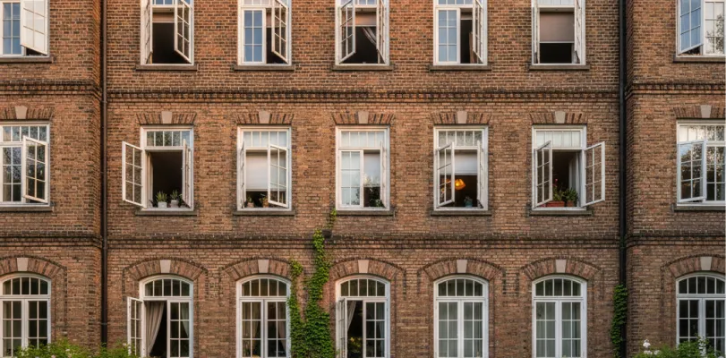 Brick residence hall facade with tall open windows, potted plants on sills and climbing ivy