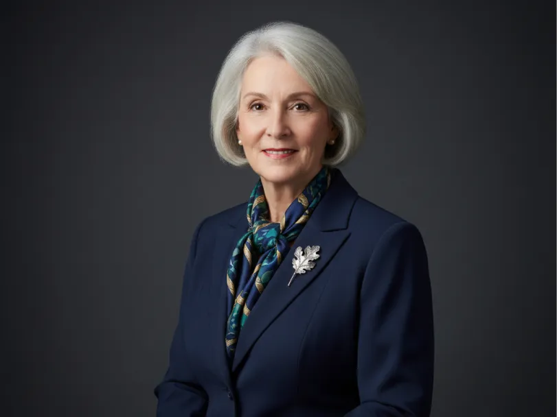 Dr. Naomi Ellsworth in a navy blazer and patterned scarf against a gray studio backdrop