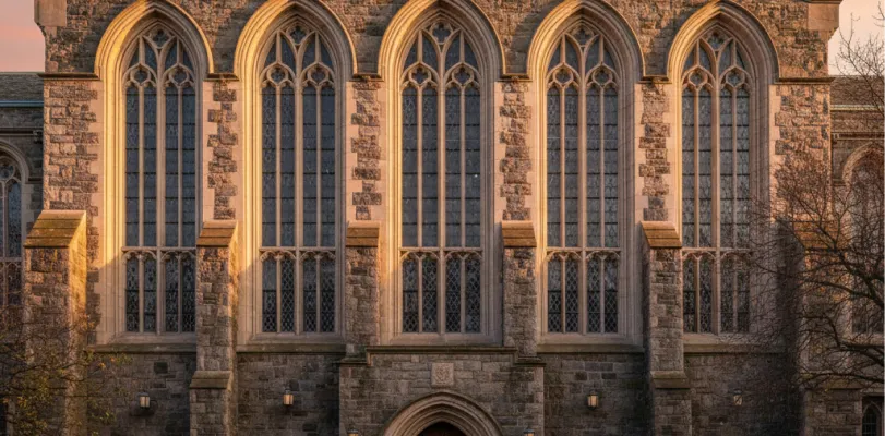 Gothic stone facade with tall tracery windows lit by low evening sun