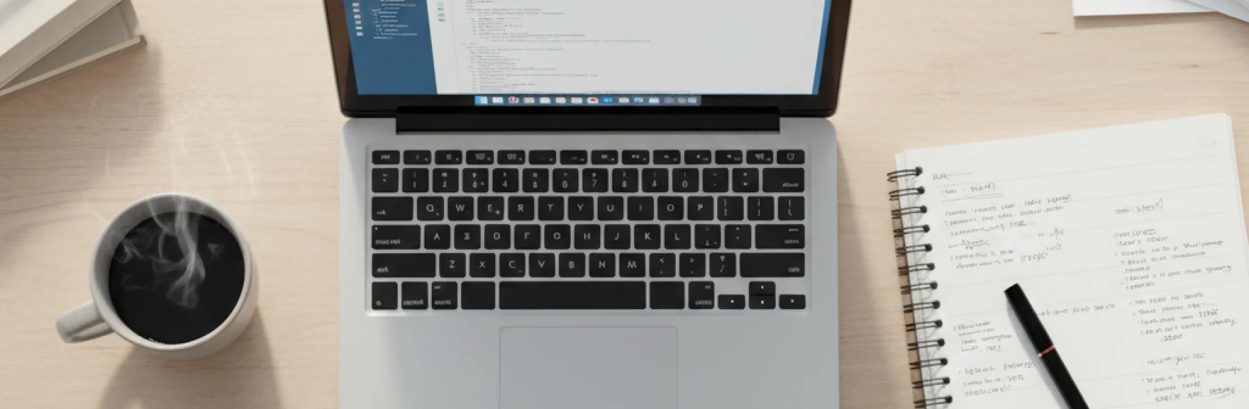 Overhead view of an open laptop, coffee mug, and handwritten notes in a spiral notebook